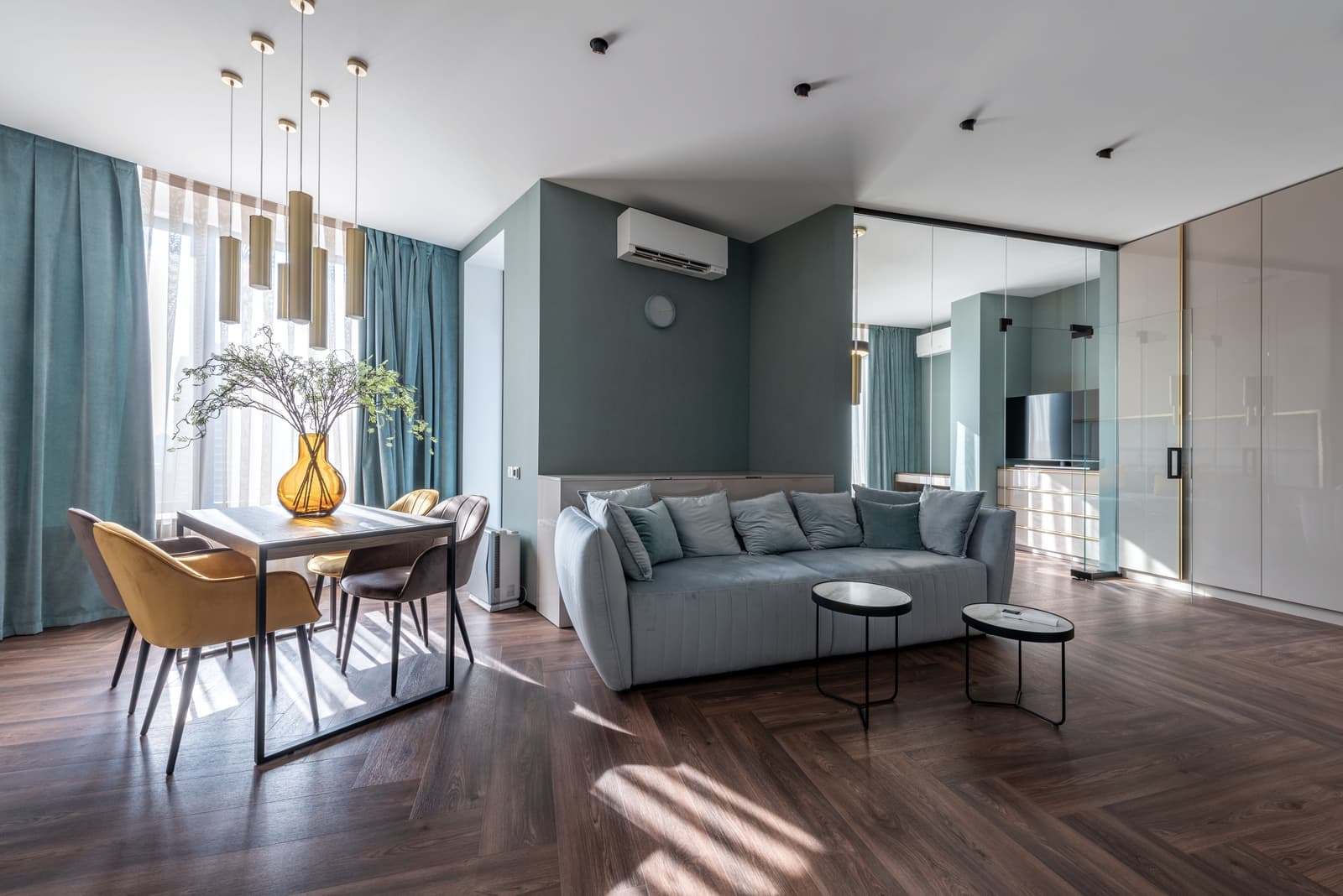 A calm apartment living room with a sofa, dining table and wooden floor in warm daylight